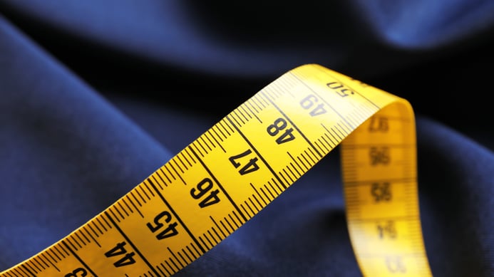 A dramatic close-up of a bright yellow measuring tape stretched diagonally across dark, tailored suiting fabric, representing precision and executive due diligence for Selkires RevOps, HubSpot CRM, and marketing agency infrastructure