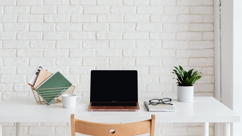 Minimal startup white desk with a laptop, notebook, glasses, and coffee cup arranged neatly against a white brick wall, representing an organized workspace